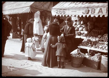 Vue de femmes avec des enfants faisant des courses à un stand de fruits et légumes au 266 7th Avenue, New York, vers 1900